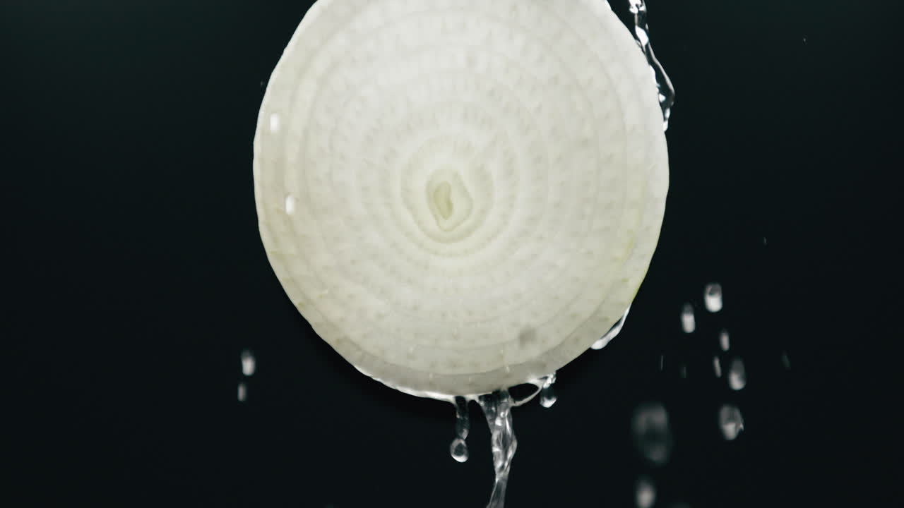 슬로우 모션 백라이트 블랙 배경에서 액체가 떨어지는 신선한 양파 슬라이스 아래로 흐르는 물