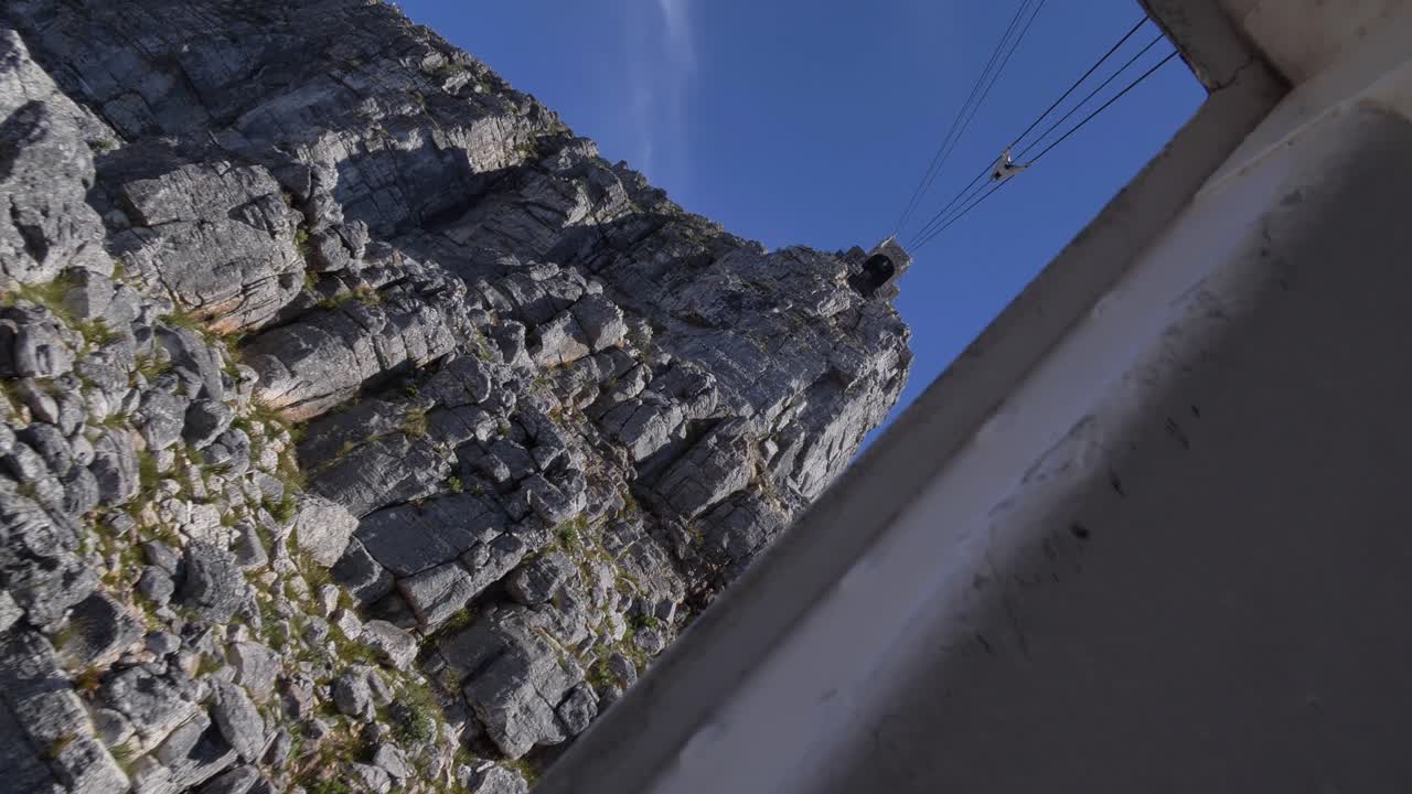 Una ripresa POV a mano libera al rallentatore dall'interno di una funivia rotante che scende lungo la parete aspra e rocciosa della Table Mountain contro un cielo blu a Città del Capo, Sudafrica.