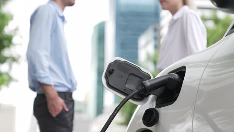 progressive businessman and businesswoman use charging station for ev car.