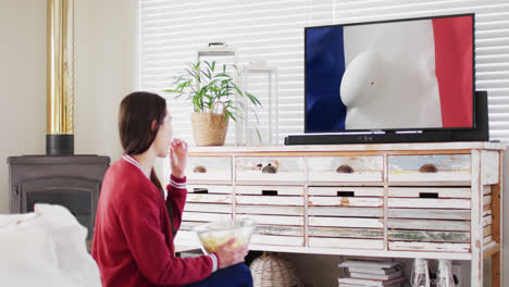 caucasian woman watching tv with rugby ball on flag of france on screen