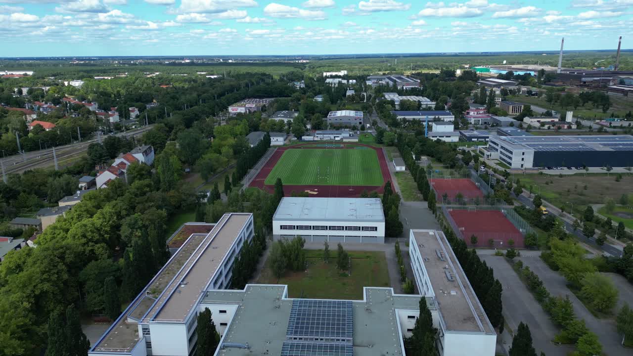 sports facilities at Hennigsdorf high school, including a soccer field, running track and other buildings in residential areas. Fantastic aerial view flight fly reverse drone