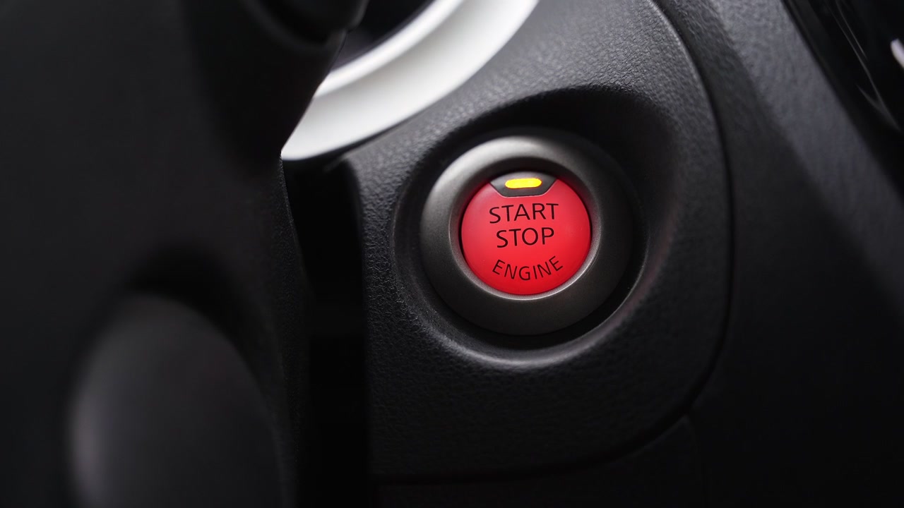 Świecący czerwony przycisk start/stop silnika na desce rozdzielczej nowoczesnego samochodu. Ujęcie wnętrza o wysokim kontraście, podkreślające technologię motoryzacyjną i systemy zapłonowe.