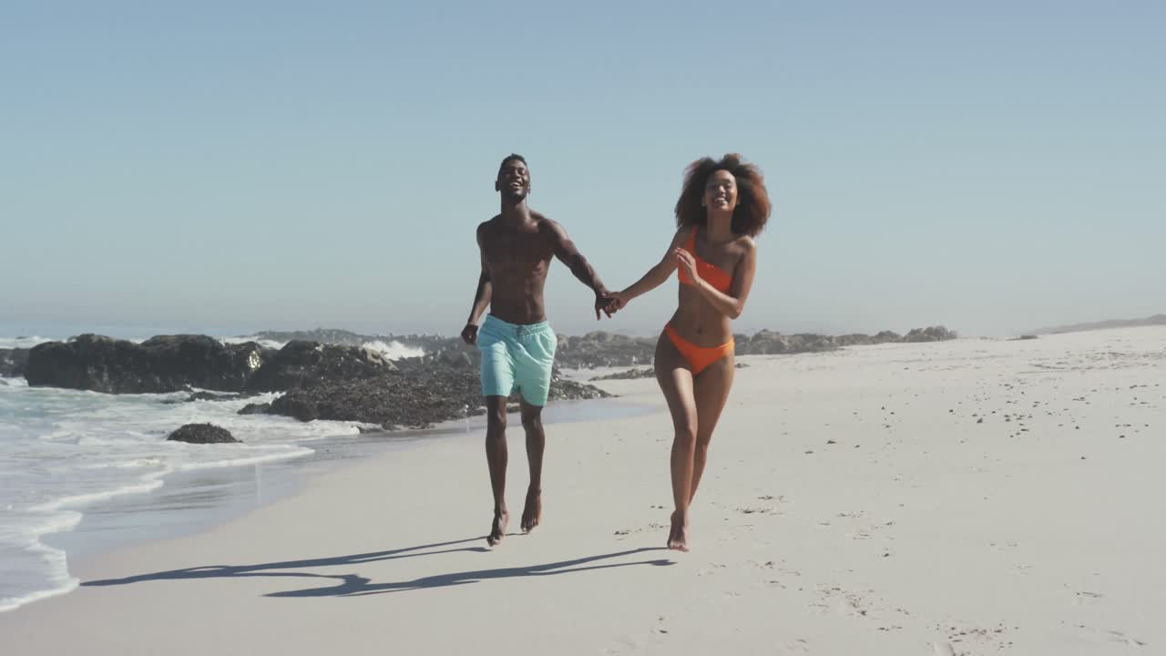 African American couple running side by side at beach