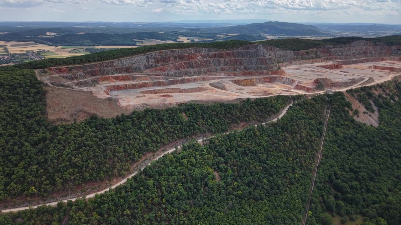 Una prospettiva aerea di una cava a cielo aperto che mostra livelli di scavo a terrazze all'interno di un terreno montuoso densamente boscoso durante le ore diurne.