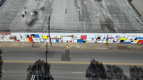 Top-down-drone-shot-of-artist-working-on-mural-on-the-side-of-a-building