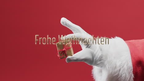 Frohe-Weihnachten-Text-über-Hand-Des-Weihnachtsmannes-Mit-Kleinem-Geschenk-Auf-Rotem-Hintergrund