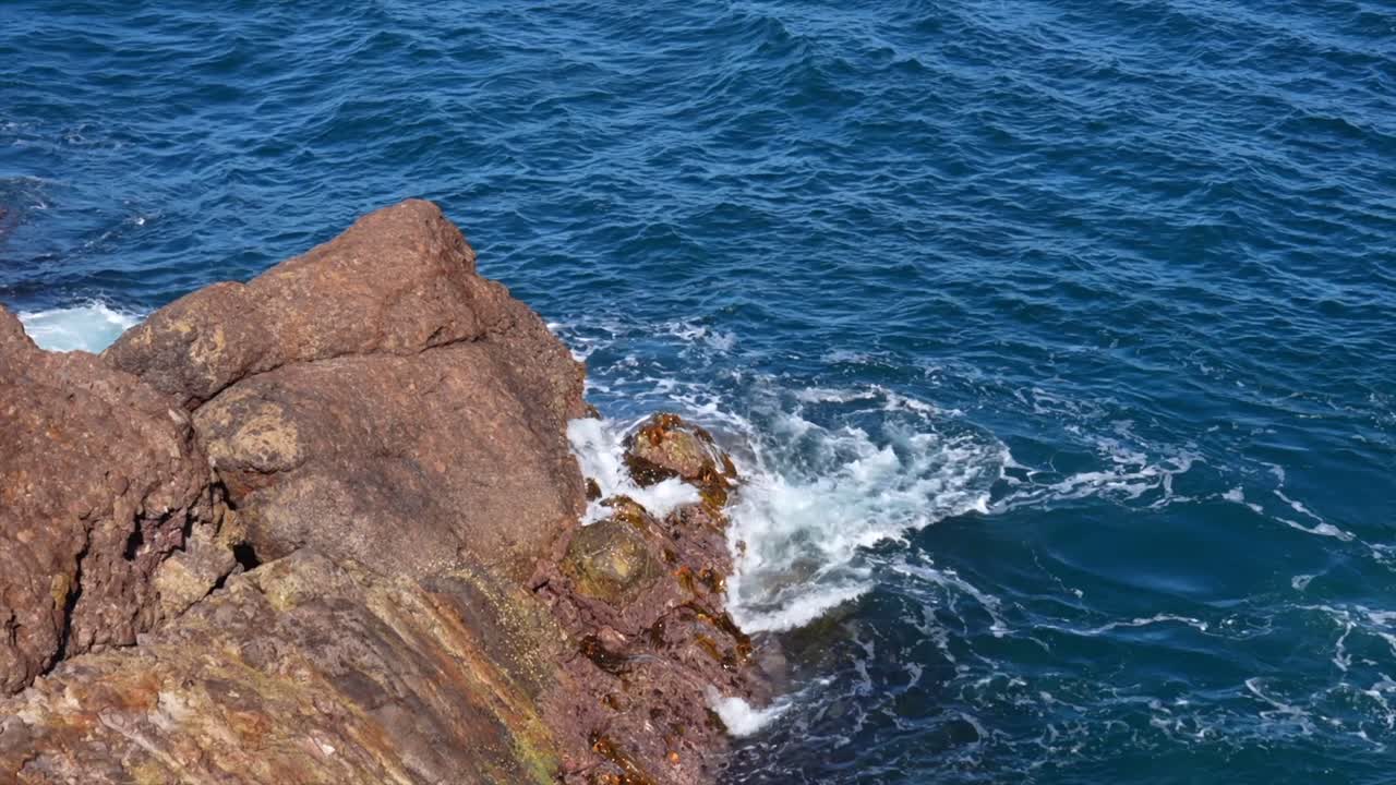 Onde dell'oceano che si infrangono contro rocce costiere con spruzzi d'acqua bianca, Tathra, Nuovo Galles del Sud, Australia.