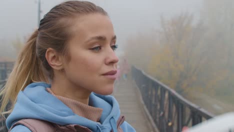 handheld close up shot of beautiful young woman putting headphones on while preparing for jog outdoors on foggy autumn morning