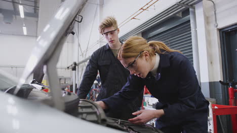 mężczyźni i kobiety patrzą na silnik samochodu na kursie mechanika samochodowego w college'u.