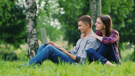 Antes-De-Trabajar-En-La-Computadora-Portátil,-El-Hombre-Abre-La-Pantalla-De-Una-Computadora-Portátil-Sentada-En-El-Césped-Del-Parque-W