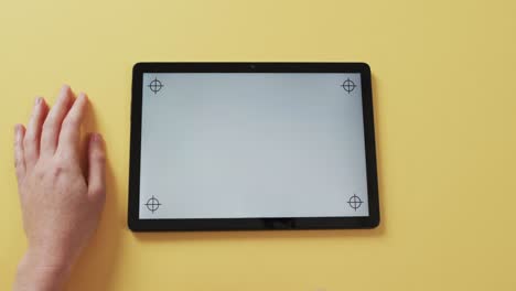 video of hands of caucasian woman and tablet with blank screen on yellow background