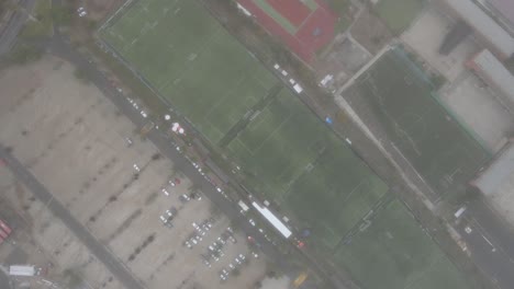 misty morning fog gradually dissipating, unveiling soccer fields and parking lot from elevated aerial perspective, revealing urban landscape with serene stillness