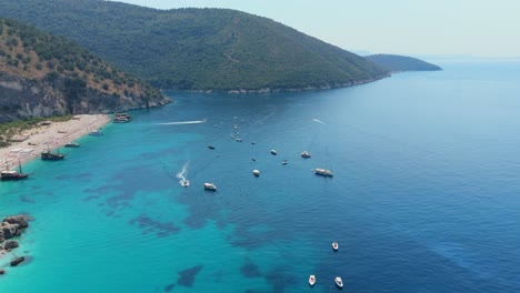 los barcos flotan en las aguas cristalinas de color turquesa cerca de una tranquila playa a lo largo de la costa albanesa.