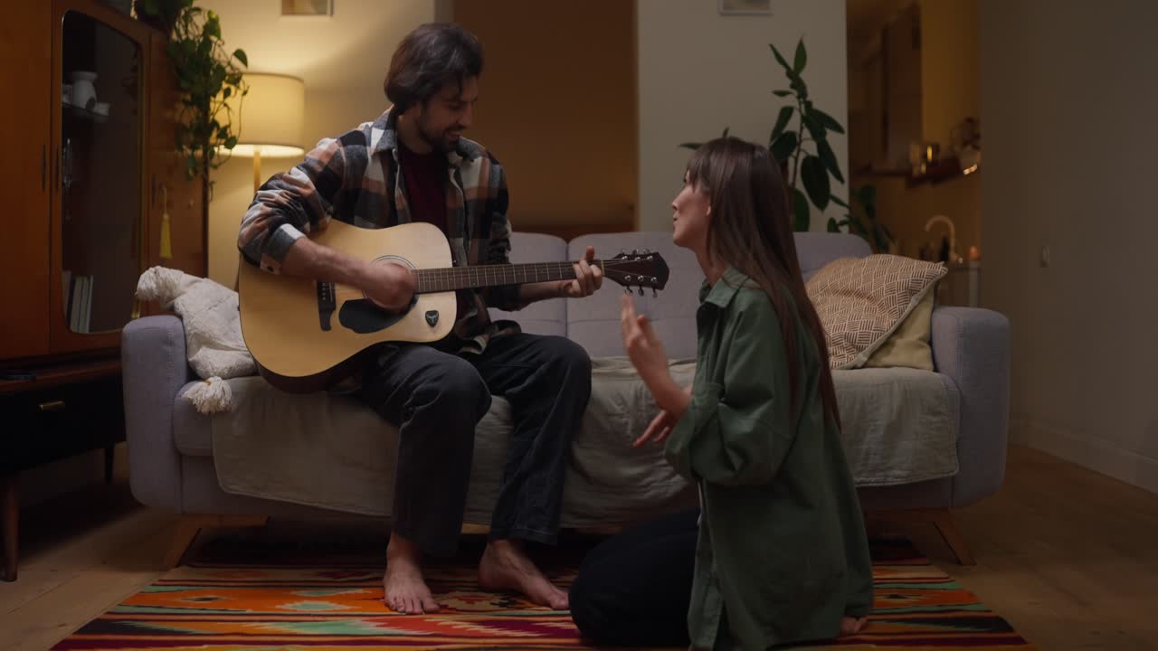 Man playing guitar for woman in living room