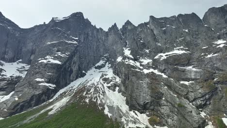 Exploring-Norway-Majestic-Troll-Wall-in-Springtime-Splendor---Low-altitude-aerial-looking-up-at-famous-mountain-wall-with-pointy-peaks