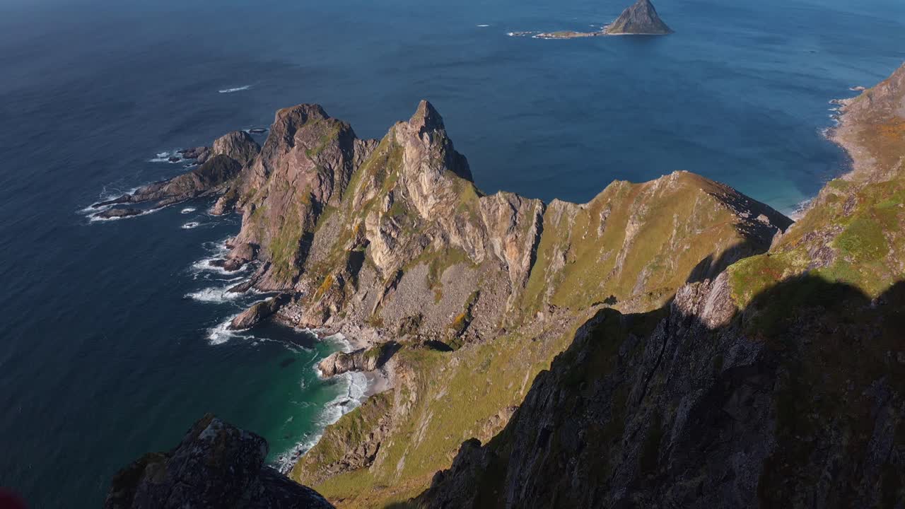 A hiker standing on a cliff, overlooking the ocean with Måtinden in the distance