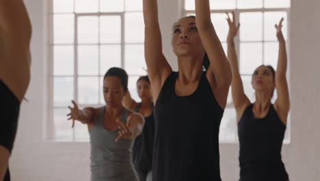 beautiful mixed race yoga woman practicing warrior pose meditation with group of multiracial women enjoying healthy lifestyle exercising in fitness studio at sunrise