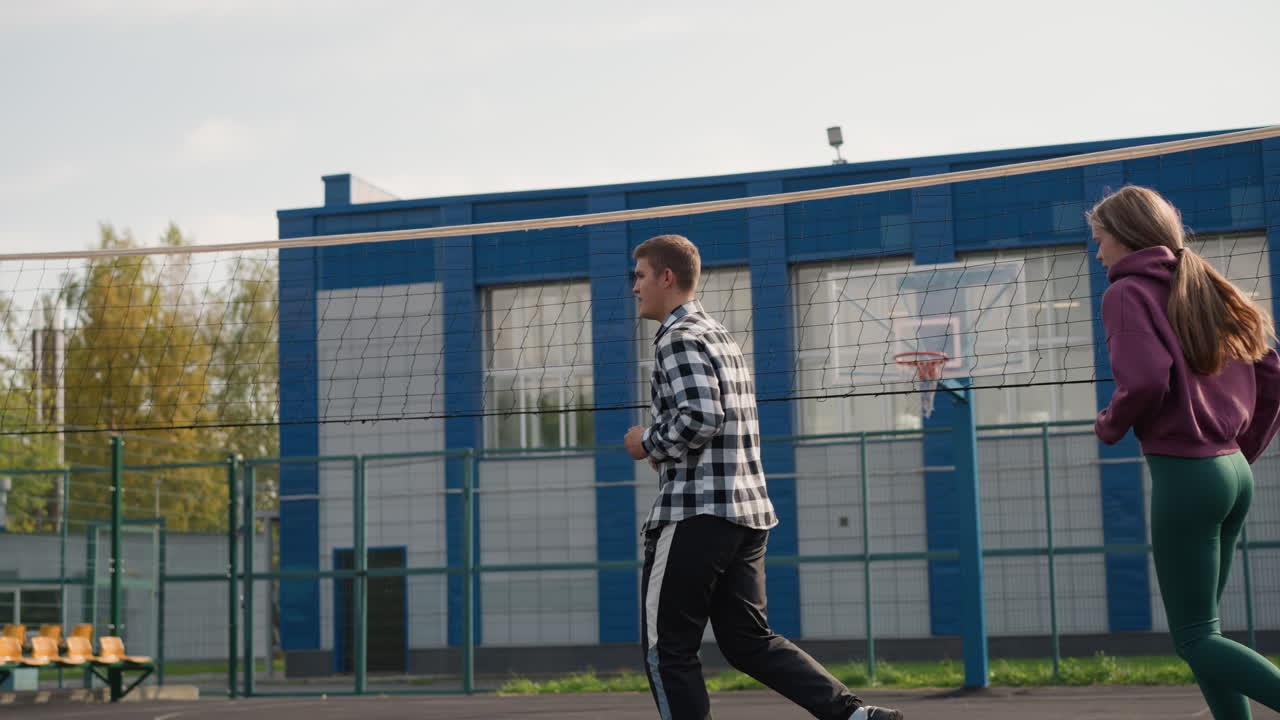Coach som veileder idrettsutøvere på utendørs volleyballbane mens de jogger, med vaiende hår og grøntområder i bakgrunnen, som fanger atletiske bevegelser i en sport treningsøkt