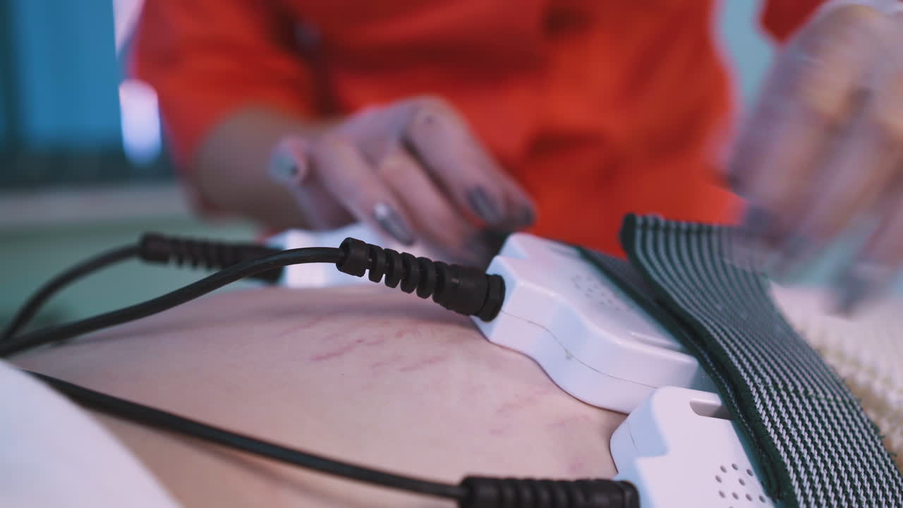la esteticista controla los electrodos en el vientre de la mujer en la clínica