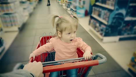 un niño pequeño se sienta en un carrito bosteza su padre rueda a lo largo de los estantes con mercancías en la tienda