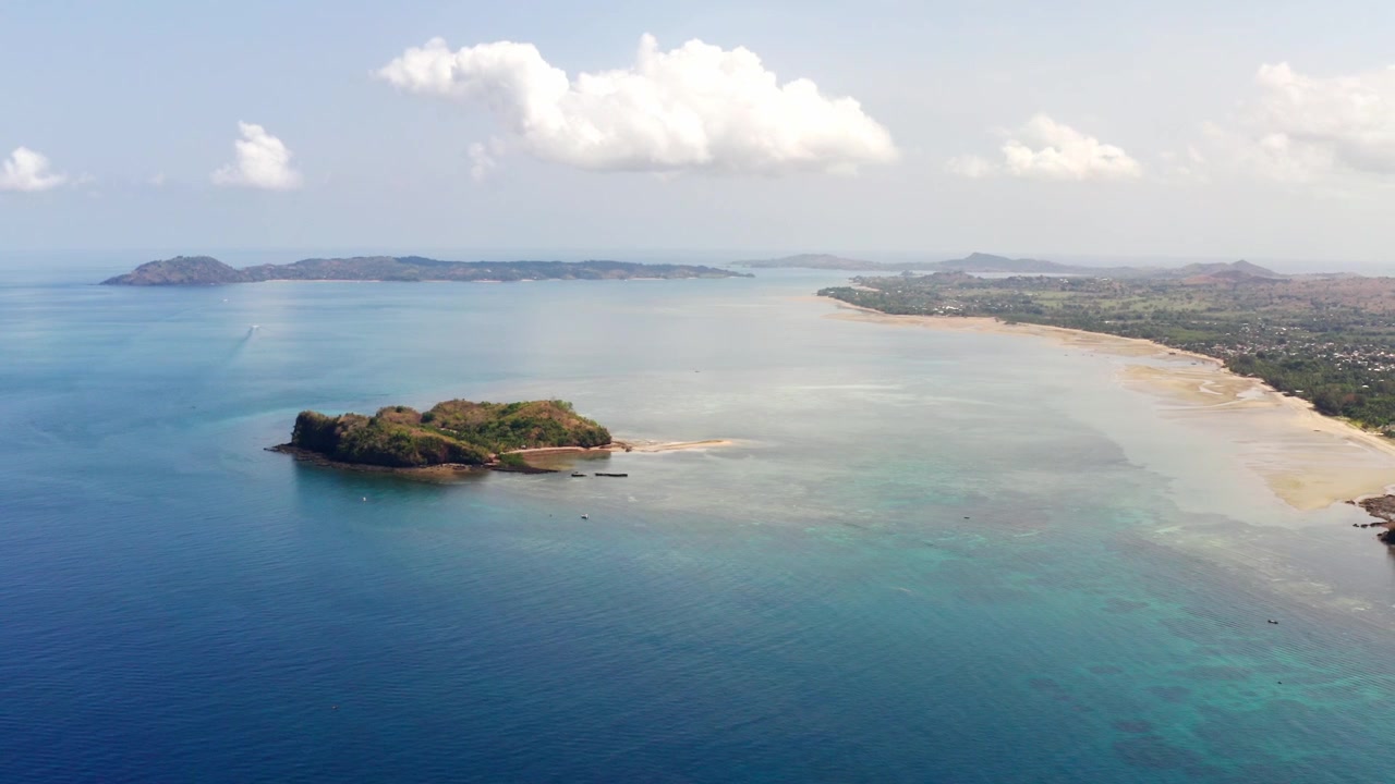 Vista aerea con drone dell'isola di Nosy Be in Madagascar durante una giornata di sole; l'oceano blu e la costa della spiaggia riflettono le nuvole di fronte a Dzamandzar; Nosy Tanga e Nosy Sakatia nell'inquadratura.