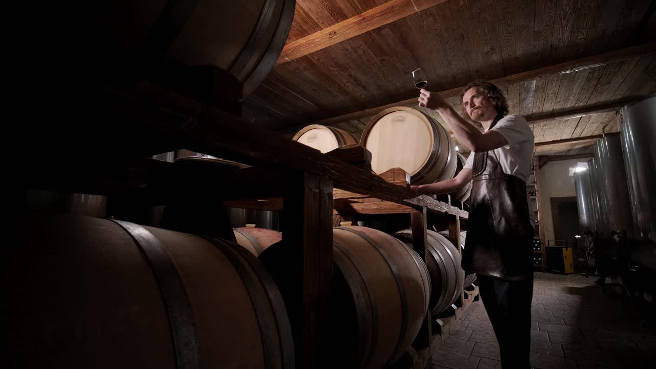 성공한 남성 소멜리어의 진정한 은 맛을 맛보고 와인 지하실에서 투명한 유리통에 부어 놓은 화이트 와인의 품질을 확인하는 것입니다.