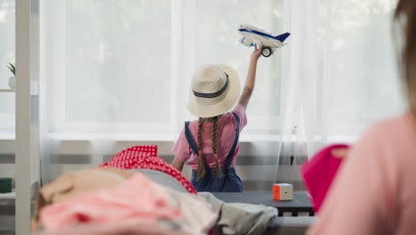 la niña juega con el avión mientras la madre dobla la ropa en el sofá