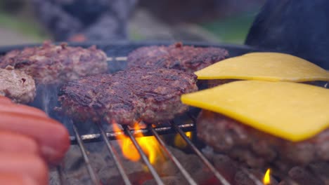 una mano de personas mientras colocan queso en hamburguesas cocinando en una parrilla de fumar