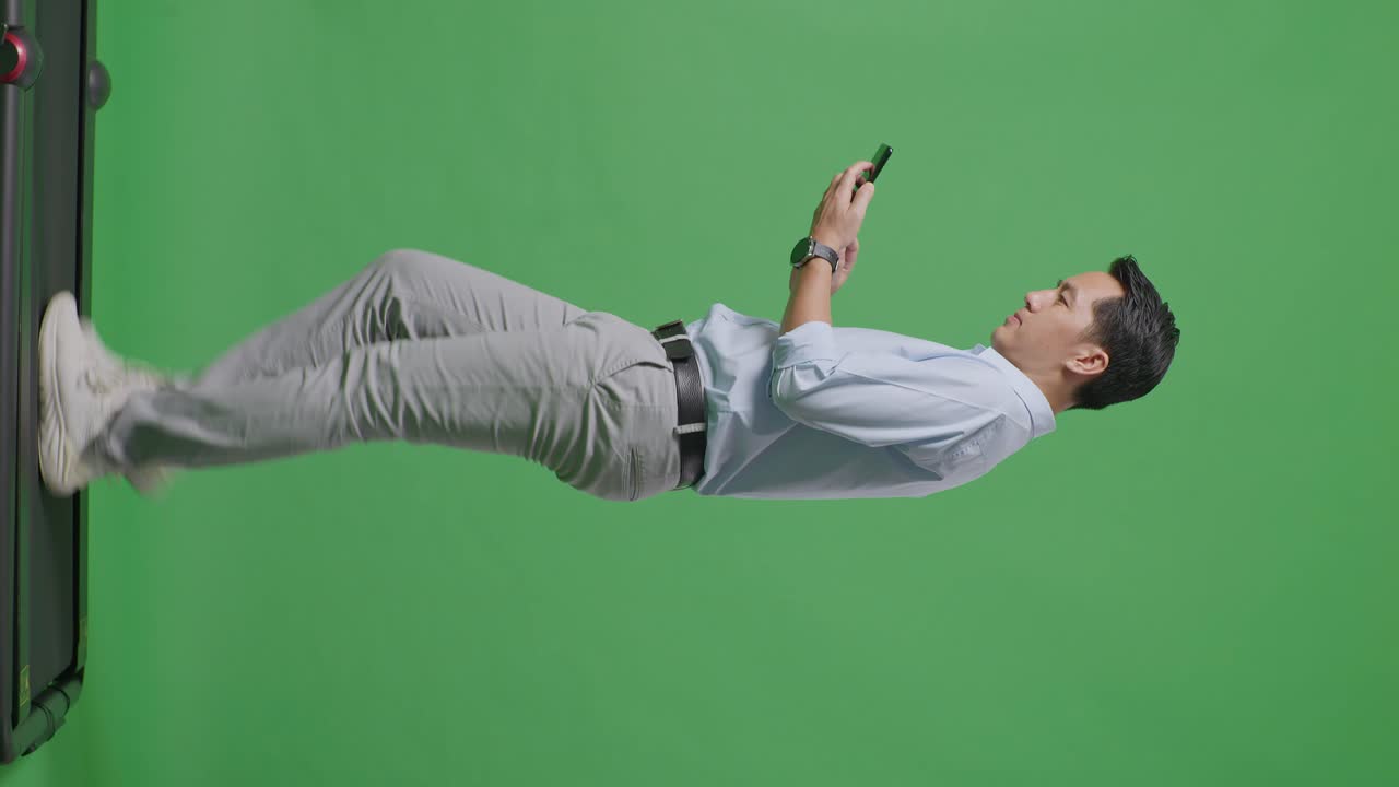 스튜디오에서 녹색 화면 배경에서 는 동안 휴대 전화를 사용하는 아시아 사업가의 전체 몸의 측면 뷰