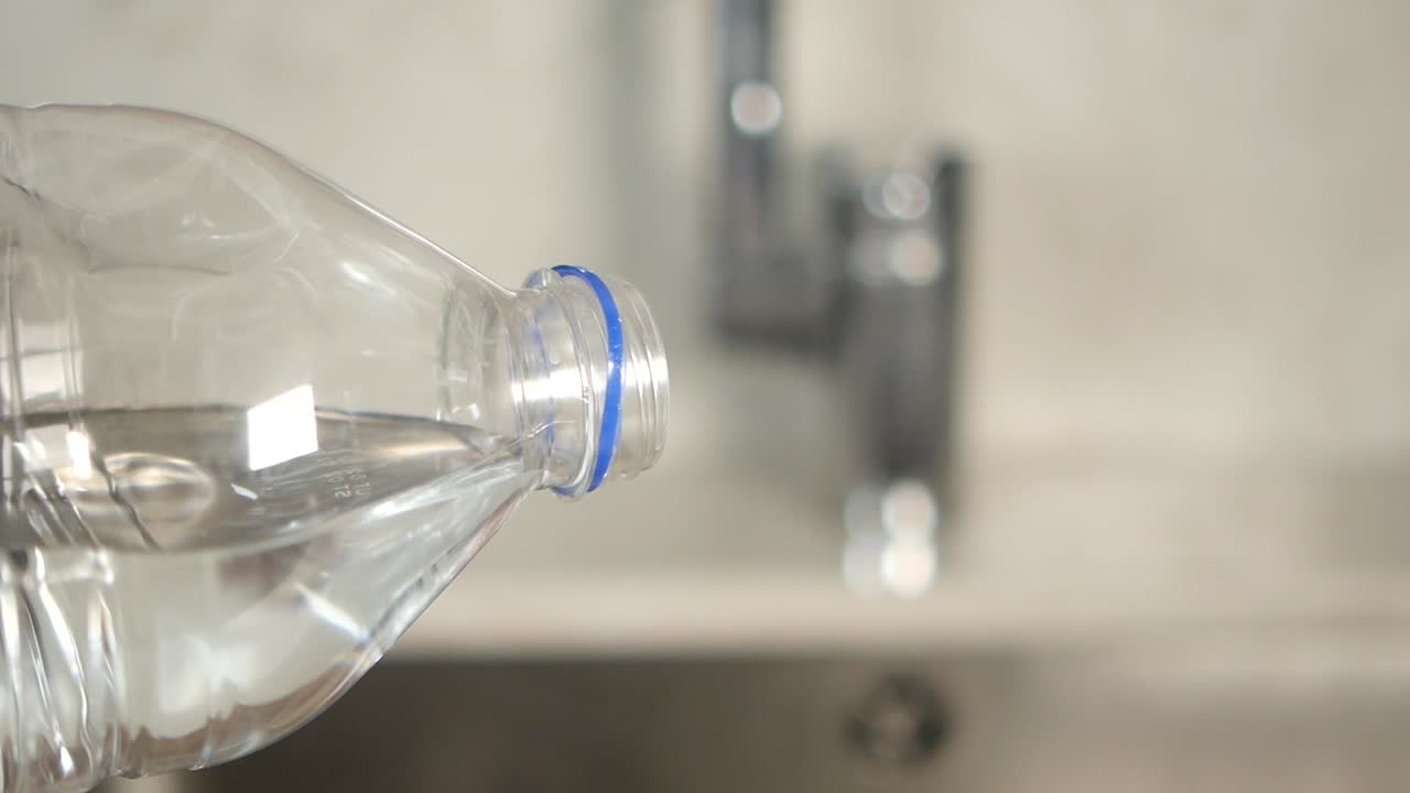 vertiendo agua de una botella de plástico en un fregadero de la cocina