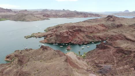 Filmische-4K-Drohnenaufnahmen-Zeigen-Eine-Große-Gruppe-Von-Booten-Und-Menschen,-Die-Sich-Im-Urlaub-Im-Sonnigen-Sommer-Am-Lake-Havasu-In-Arizona-Und-Kalifornien-Beim-Klippenspringen-Und-Schwimmen-Vergnügen