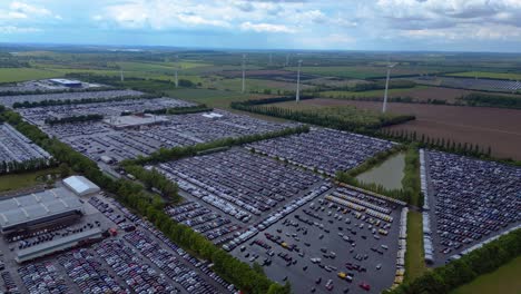 large parking lot full of cars near a wind farm and countryside in germany. spectacular aerial view flight drone shot footage from above