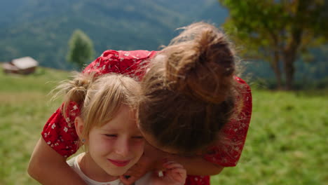 Madre-Besando-A-Su-Hija-En-El-Prado-En-Un-Día-Soleado-De-Cerca.-Mujer-Abrazándose-Con-Un-Niño.