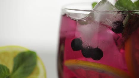 Stiring-in-a-glass-with-cold-drink,-leaves-of-mint,-lime,-lemon,-currants,-ice