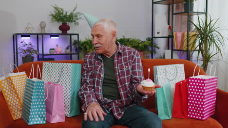 feliz anciano anciano abuelo hombre celebrando fiesta de cumpleaños, hace un deseo soplando vela ardiente