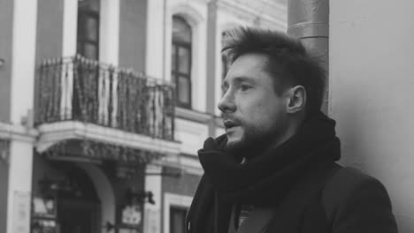 black and white and close up view of a man in coat singing and playing guitar in the street 1