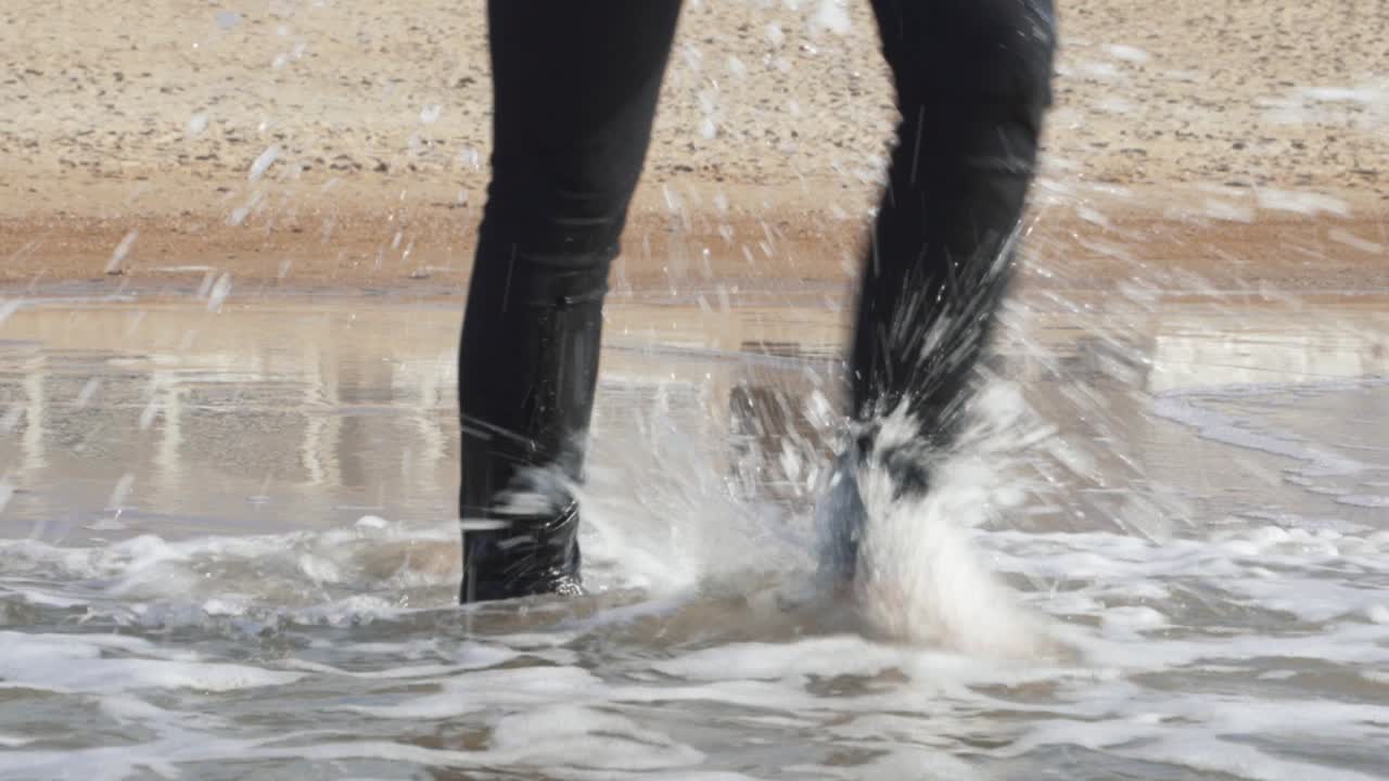 Legs in wet black pants of a woman walking in water of the sea, barefoot
