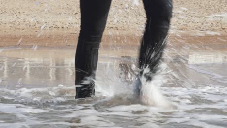 Piernas-En-Pantalones-Negros-Mojados-De-Una-Mujer-Caminando-En-El-Agua-Del-Mar,-Descalza