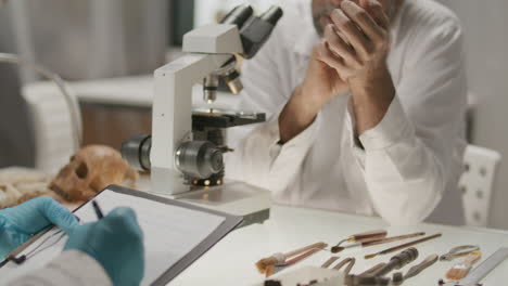 senior archaeologist taking notes during research with colleague in laboratory