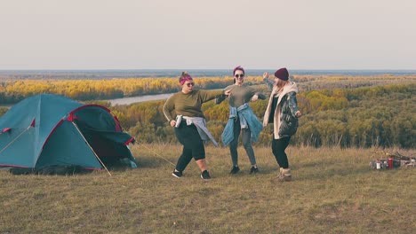 happy young women dance in campsite on calm river bank