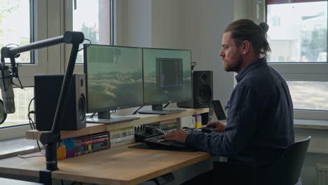 Dive-into-a-modern-work-scene-as-a-ponytailed-man-focuses-on-his-computer-at-the-desk