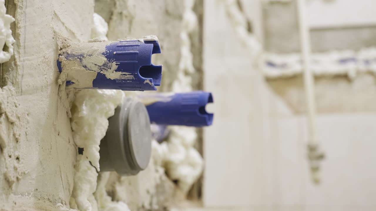 un primer plano de las tuberías de agua de plástico azul que sobresalen de la pared del baño, la pared desnuda mientras se preparan las provisiones para instalar un lavabo a medida que el baño se renueva