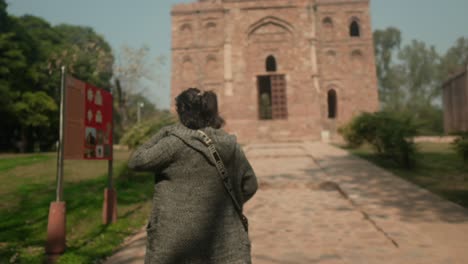 Woman-approaching-an-ancient-brick-temple-on-a-sunny-day,-backpack-in-tow,-exploring-cultural-heritage