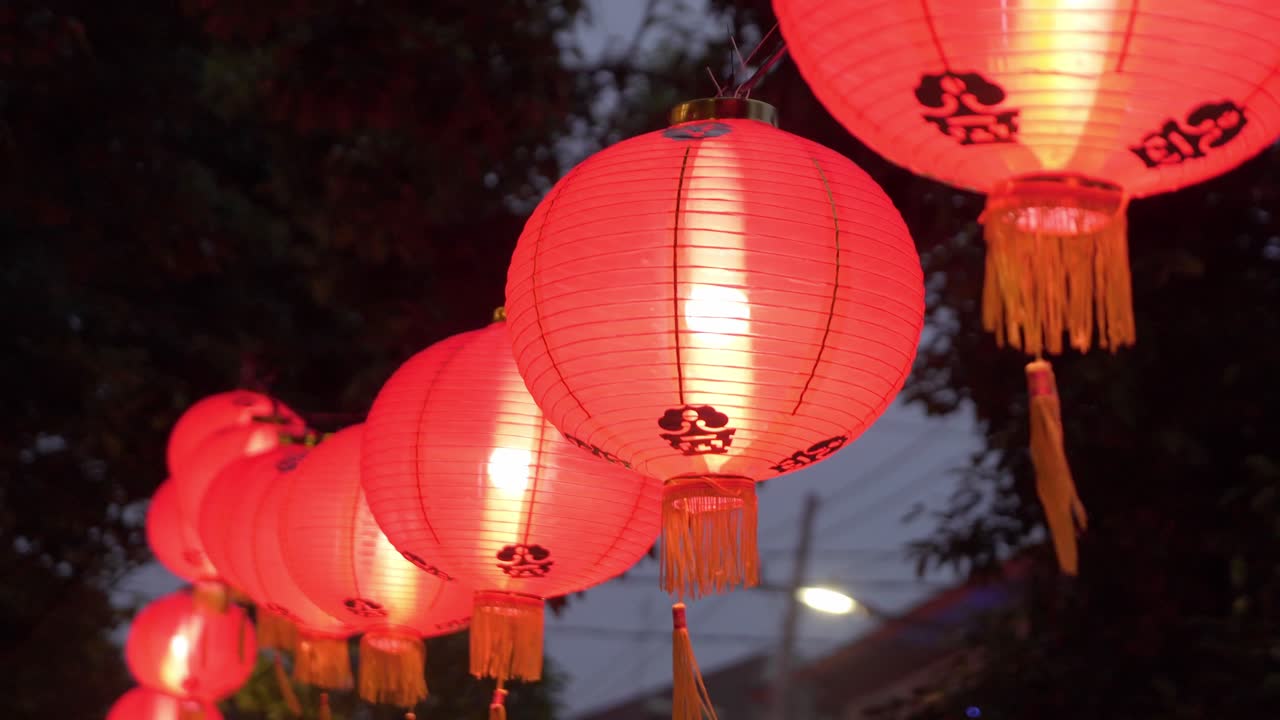 Red Chinese lanterns glowing at dusk during festival, hanging outdoors with trees in background