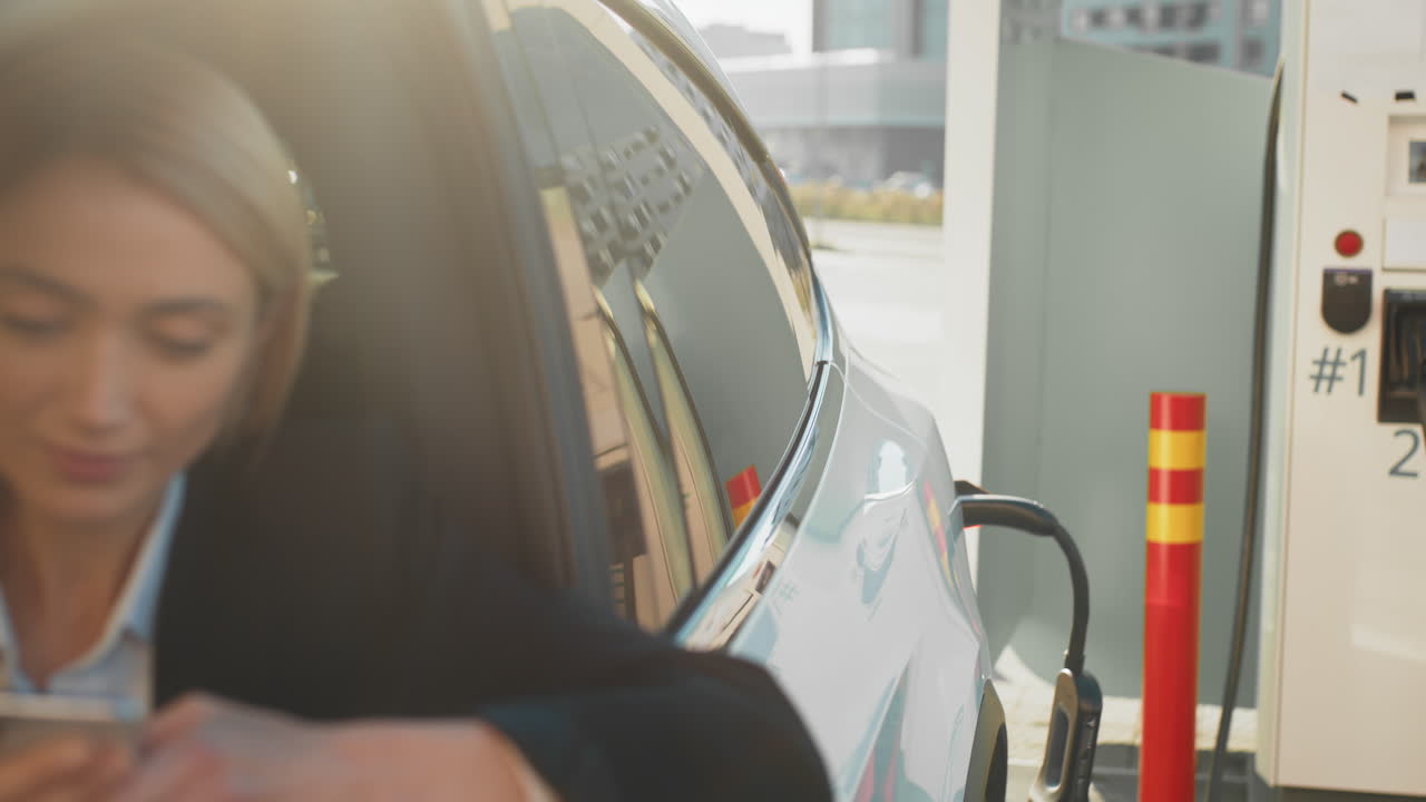 전기 차량을 충전하는 동안 전화를 사용하는 여성