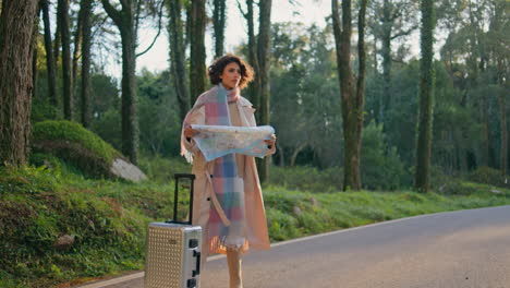 girl tourist studying map on scenic forest roadside with suitcase. woman journey