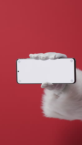 vertical video of santa claus holding smartphone with copy space on red background