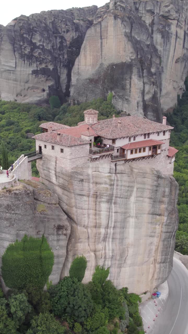 Vertical aerial arc of a cliff-top monastery perched on a massive rock column in Meteora, Greece