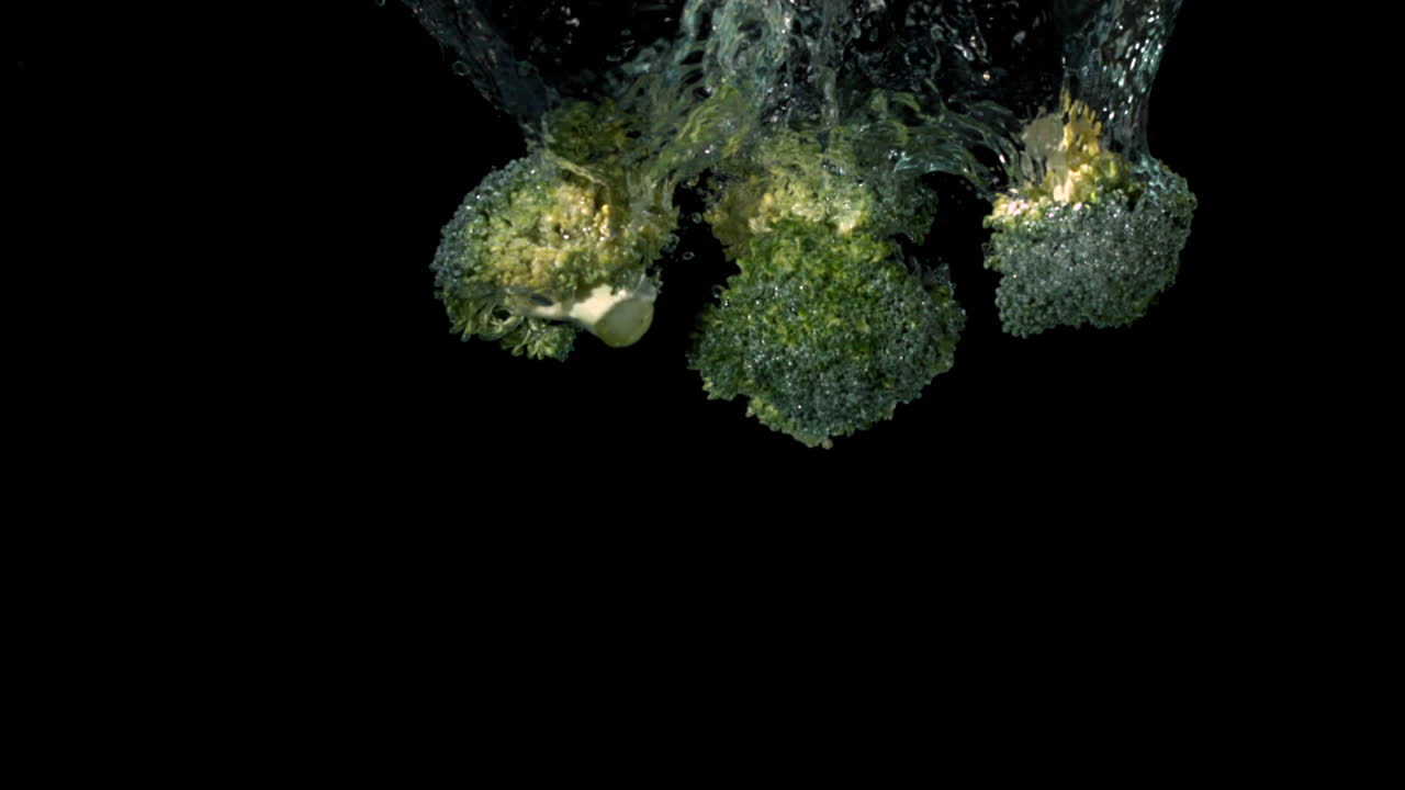Broccoli florets falling in water on black background