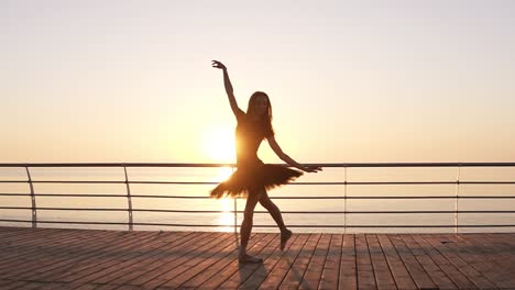 Attraktive-Ballerina-Übungen-Im-Stretching.-Klassische-Ballettbewegungen-Ausführen.-Langhaariges-Junges-Mädchen-Im-Dunklen-Tutu.-Damm-In-Der-Nähe-Des-Meeres-Oder-Ozeans.-Sonne-Scheint.-Zeitlupe